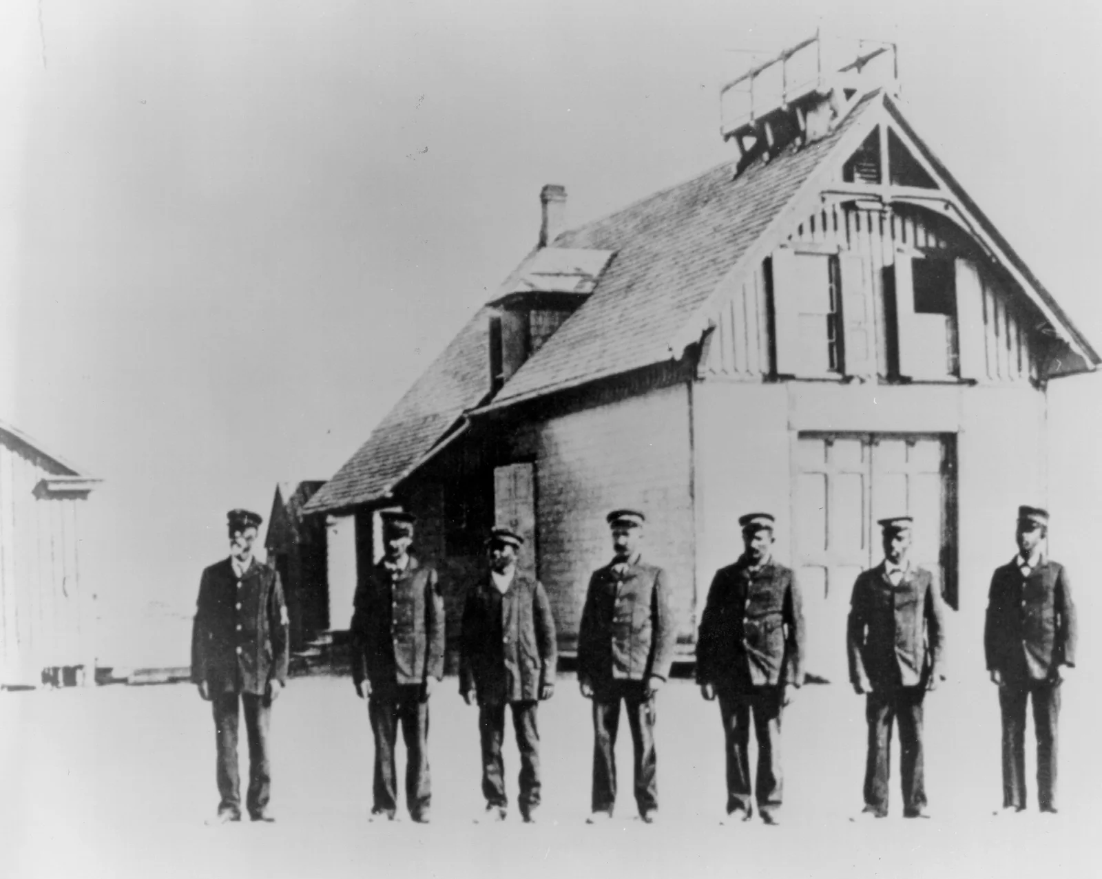 Richard Etheridge and six Pea Island surfmen standing outside their wooden lifesaving station in an archival black-and-white photograph